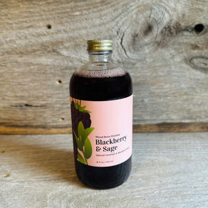 Glass jar containing blackberry sage drink mixer on barnwood background